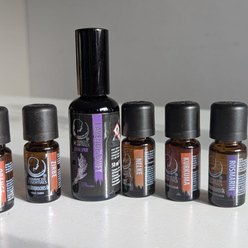 Fünf ätherische Öle und ein Lavendelspray von Advanced Essentials in Braunglasflaschen – natürliche Bio-Qualität im Sonnenlicht auf weißem Hintergrund.