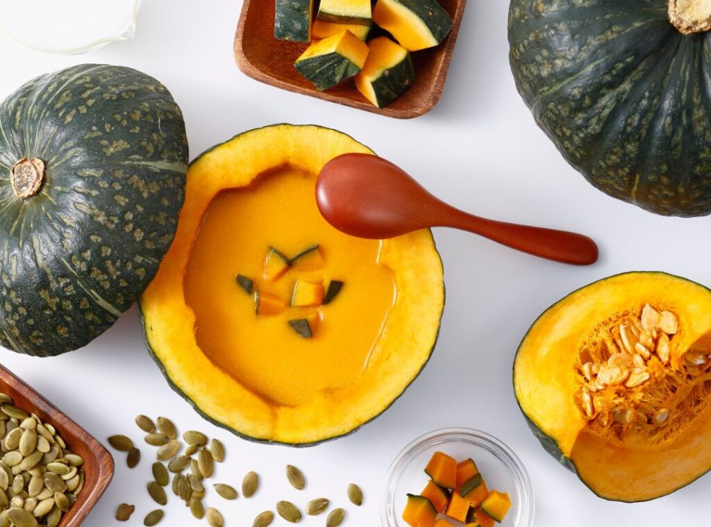 Cremige Kürbissuppe im ausgehöhlten Kürbis serviert, mit Kürbiskernen und frischen Kürbisstücken als Zutaten.